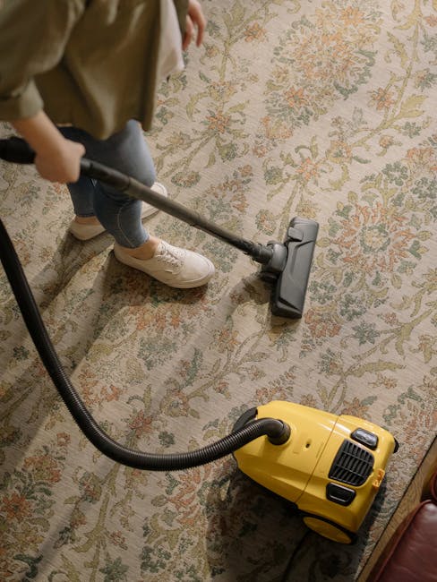 Three professional cleaners from Carpet Cleaning Hammersmith are positioned in a modern living room, engaged in surface cleaning activities. The room features a light-colored wooden floor and a dark-c